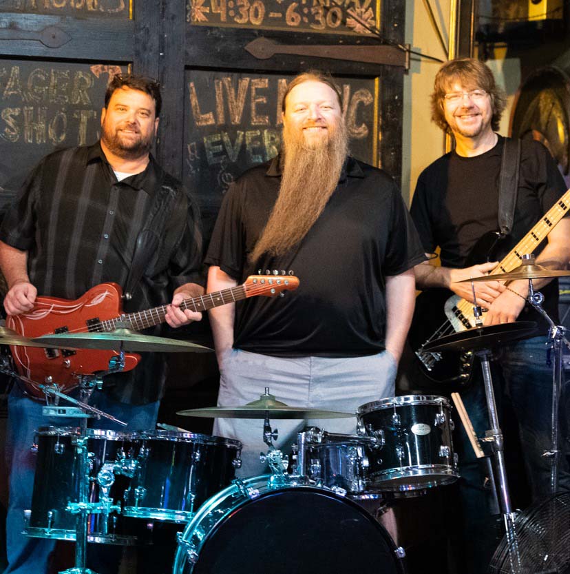 Members of the Paul Roper Band standing in front of drum set holding guitars
